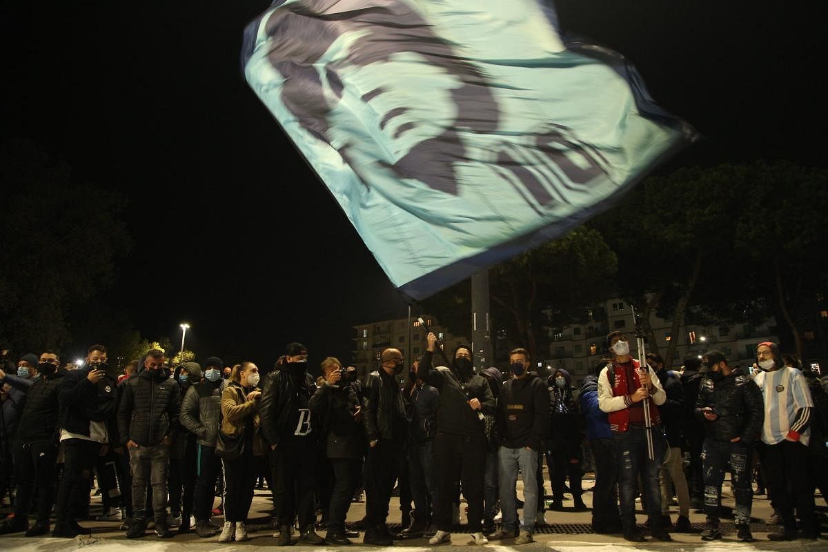 People gather at the main entrance of the San Paolo stadium in Naples on November 25, 2020 waving a flag at the effigy of Argentinian football legend Diego Maradona, to mourn after the annoucement's of Maradona's death. Credit: AFP