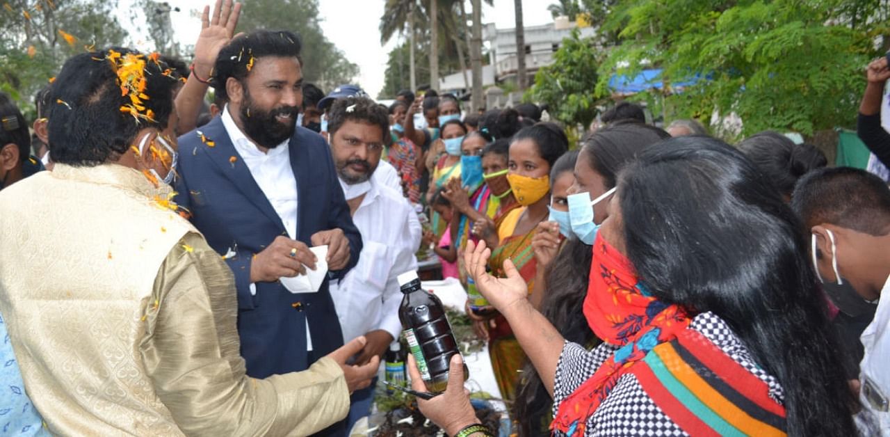 Minister B Sriramulu interacts with the tribals about the herbal hair oil, at Pakshirajapura tribal hamlet in Hunsur taluk on Thursday. Credit: DH.
