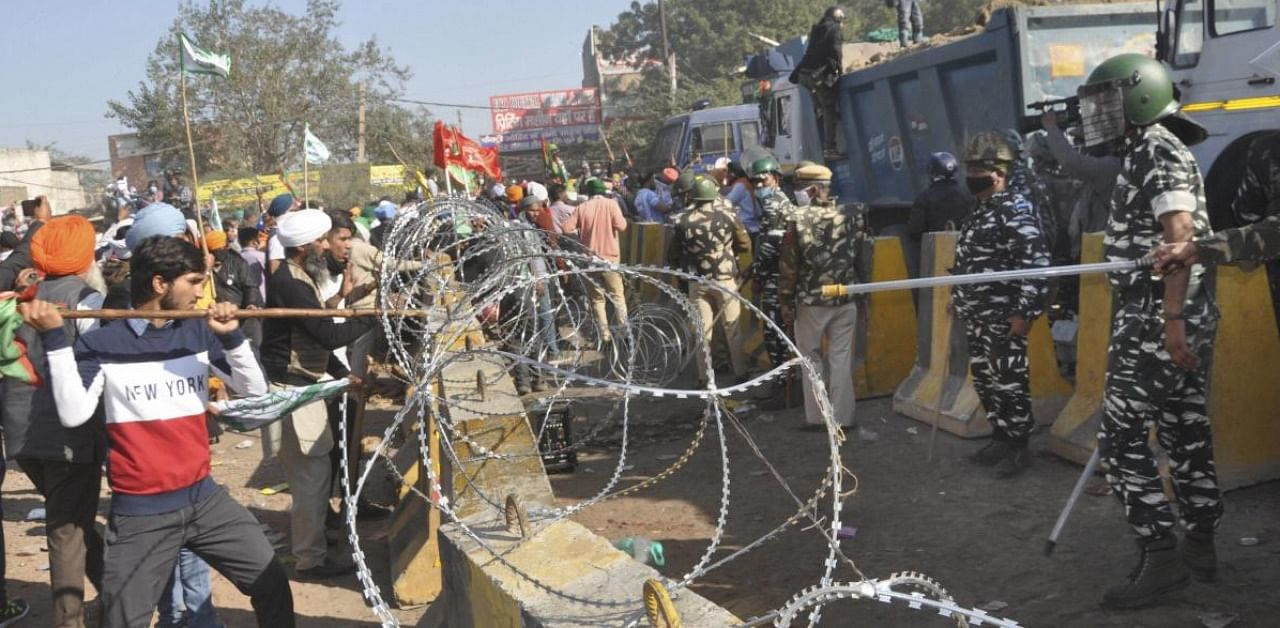 Farmers heading towards Delhi try to break the barricades during their 'Delhi Chalo' protest march against the new farm laws, at Kundli border in Sonepat. Credit: PTI.