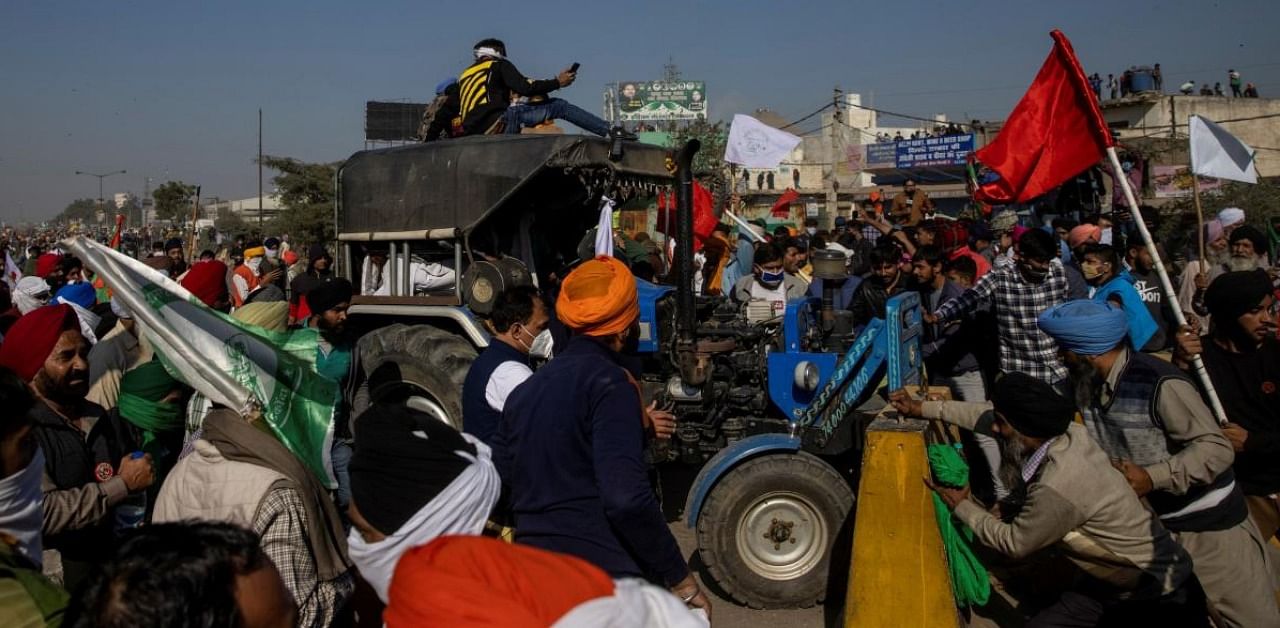 Farmers use a tractor to remove concrete barriers set up to stop them from entering the national capital Delhi during a protest against the newly passed farm bills, at Singhu border. Credit: Reuters.