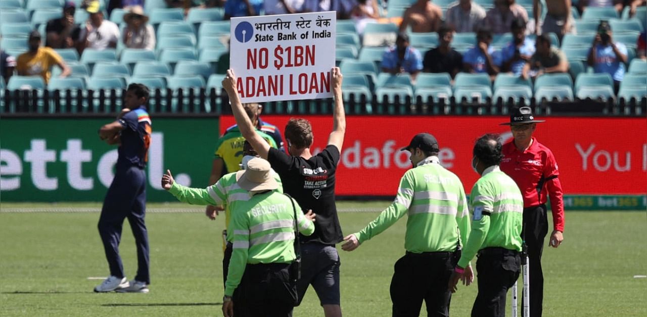 A protester who disrupted the game with a sign that reads "No $1BN Adani Loan" is escorted off the field by security. Credit: Reuters Photo