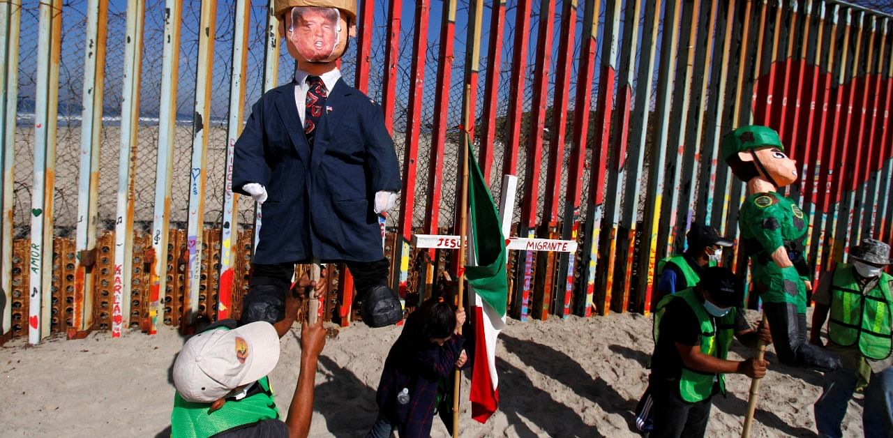 Migrants and members of civil society hold pinatas in the image of US President Donald Trump and a border patrol officer during a protest against stalled asylum claims and the building of the wall, at the border fence between Mexico and the US. Credit: Reuters Photo