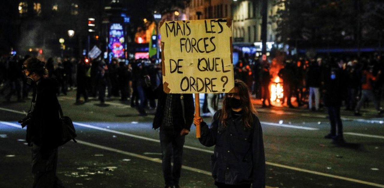 A woman holds a placard reading "But the force of what order" as she takes part in a demonstration in Paris, to protest against the "global security" draft law, which Article 24 would criminalise the publication of images of on-duty police officers with the intent of harming their "physical or psychological integrity". Credit: AFP
