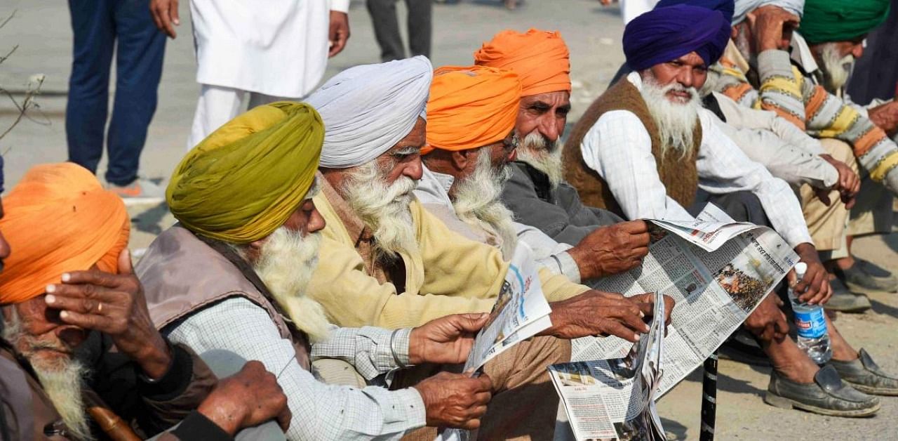 Farmers read newspapers at Singhu border during their ongoing protest march 'Delhi Chalo' against Centre's new farm laws. Credit: PTI.