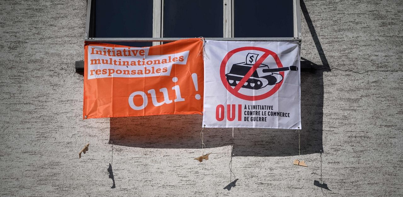 This photograph taken on November 22, 2020 in Lausanne, shows two campaign banners reading "Responsible business initiative, Yes!" (L) and "Yes to the initative against investments in weapon firms". Credit: AFP Photo