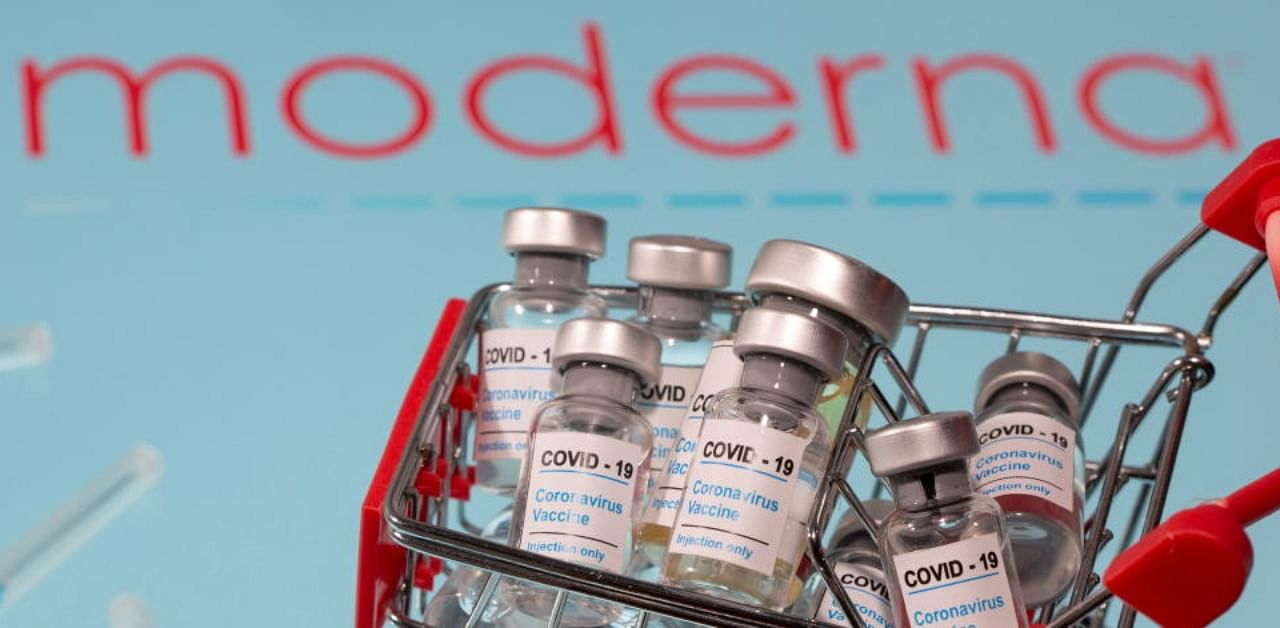 A small shopping basket filled with vials labeled "COVID-19 - Coronavirus Vaccine" and medical sryinges are placed on a Moderna logo. Credit: Reuters Photo