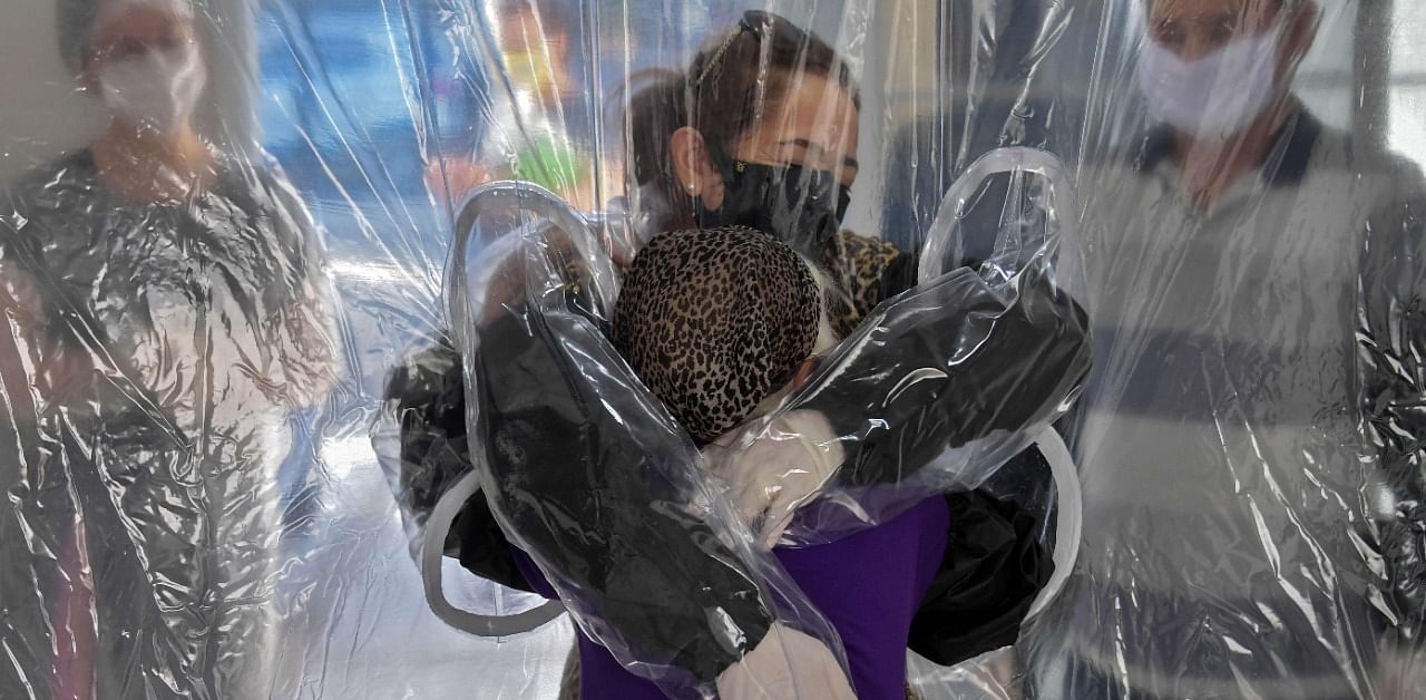 Elisabete Nagata (top) hugs her 76-year-old sister-in-law Luiza Nagata, through a transparent plastic curtain at a senior nursing home in Sao Paulo, Brazil. Credit: AFP Photo