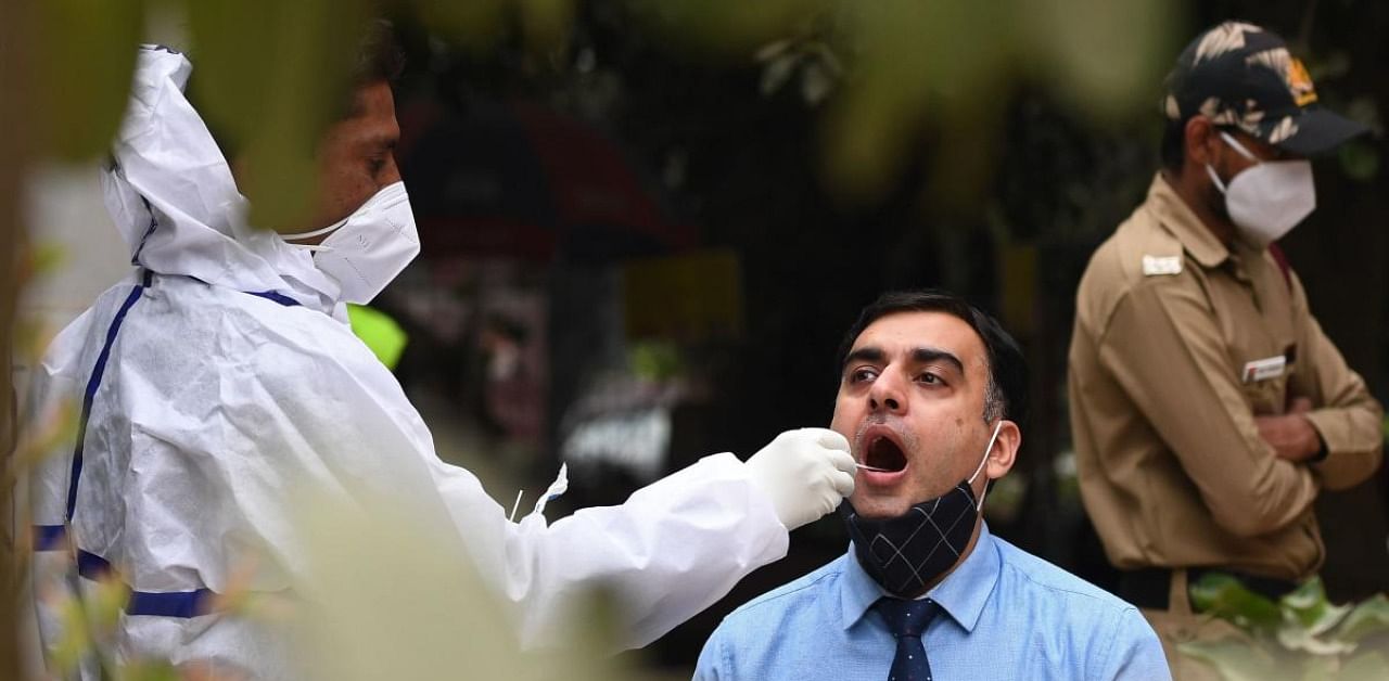 A health worker wearing protective gear collects a swab sample from a man for a RT-PCR test for the Covid-19 at a marketplace in New Delhi. Credit: AFP Photo