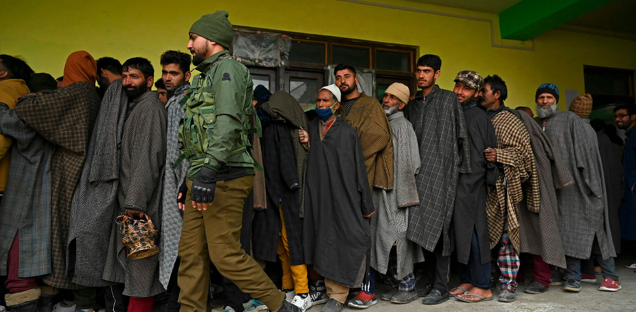 An Indian paramilitary soldier walks past voters standing in a queue to cast their ballots during the second phase of the District Development Council (DDC) and Panchayat by-elections at a polling station in Ganastan Sumbal area of Bandipora district on December 1, 2020. Credit: AFP Photo