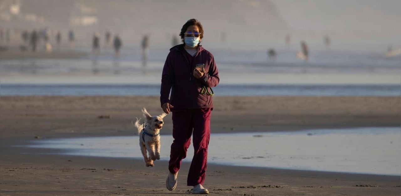A woman wears a face mask as she walks her dog along the beach during the outbreak of the coronavirus disease (COVID-19) in Del Mar, California, US, December 1, 2020. Credit: Reuters Photo