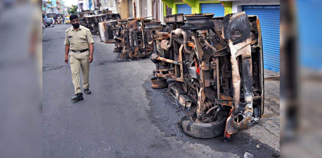 A policeman walks past vehicles burnt during the riots at DJ Halli on August 11. DH File Photo/ Pushkar V