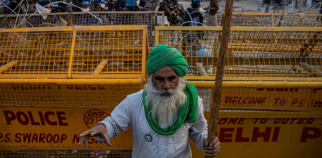 A farmer stands in front of police barricades during a protest against the newly passed farm bills at Singhu border near Delhi. Credit: Reuters Photo
