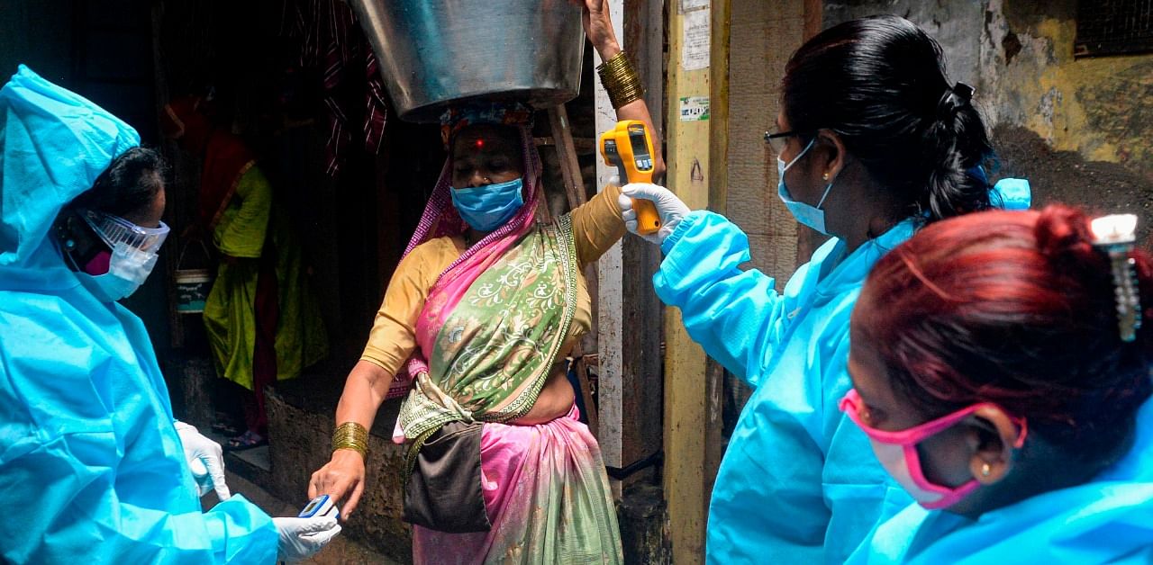 Health workers wearing Personal Protective Equipments (PPE) use a fingertip pulse oximeter and check the body temperature of a fisherwoman inside the Dharavi slum. Credit: AFP Photo