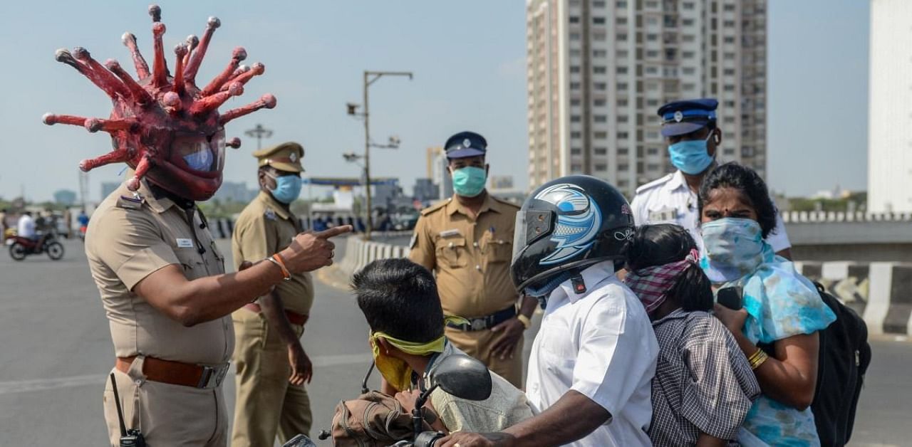 Police inspector Rajesh Babu (C) wearing coronavirus-themed helmet speaks to a family on a motorbike at a checkpoint during a government-imposed nationwide lockdown as a preventive measure against the COVID-19 coronavirus in Chennai on March 28, 2020. Credit: AFP Photo