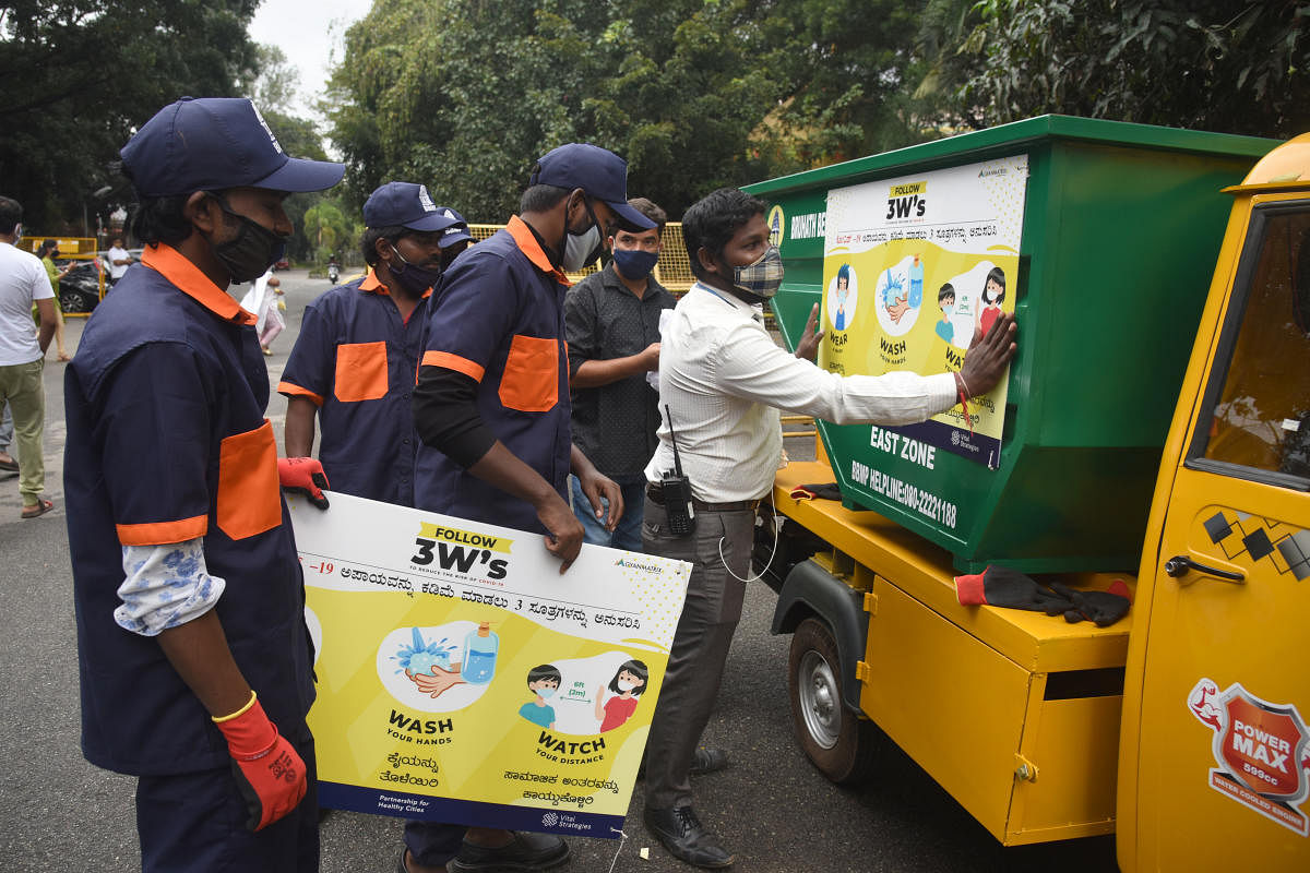 BBMP workers stick posters on garbage trucks at the launch of the 3Ws campaign at the Palike head office on Friday. DH Photo/S K Dinesh