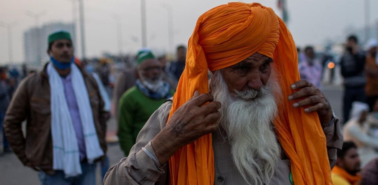 A farmer wears his scarf as he listens to a speaker on a blocked highway as they attend a protest against the newly passed farm bills at the Delhi-Uttar Pradesh border in Ghaziabad. Credit: Reuters Photo