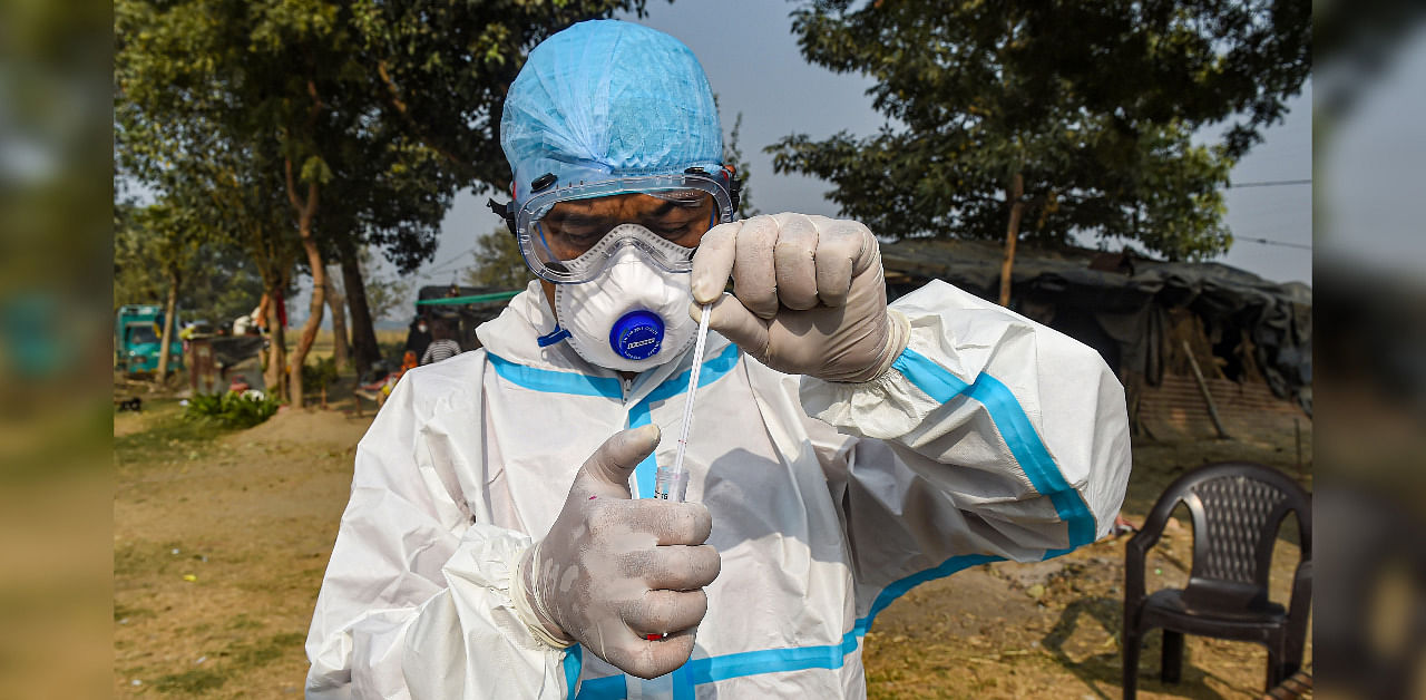A health worker, wearing protective gear, shows a swab sample collected from Vijay Ghat slum area during a Covid-19 testing camp, in New Delhi. Credit: PTI