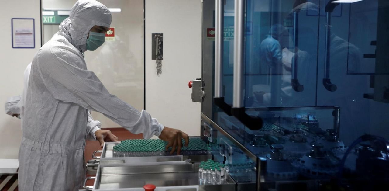 An employee in personal protective equipment (PPE) removes vials of AstraZeneca's COVISHIELD. Credit: Reuters Photo