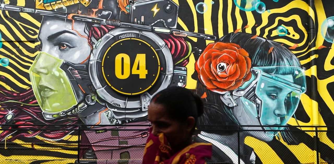 A woman walks past a graffiti of people wearing protective masks amidst the spread of the coronavirus disease (COVID-19), on the outskirts of Mumbai, India, December 9, 2020. Credit: Reuters Photo