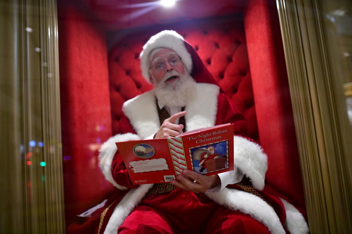 A man dressed as Santa Claus, sitting behind a plexiglass divider due to the coronavirus disease (COVID-19) pandemic, reads "The Night Before Christmas" while awaiting visitors at the Plymouth Meeting Mall in Plymouth Meeting, Pennsylvania, U.S. November 14, 2020. Credit: REUTERS