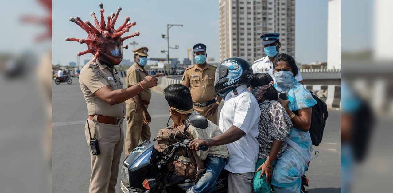 Police inspector Rajesh Babu (C) wearing coronavirus-themed helmet speaks to a family on a motorbike at a checkpoint during a government-imposed nationwide lockdown as a preventive measure against the COVID-19 coronavirus in Chennai on March 28, 2020. Credit: AFP Photo