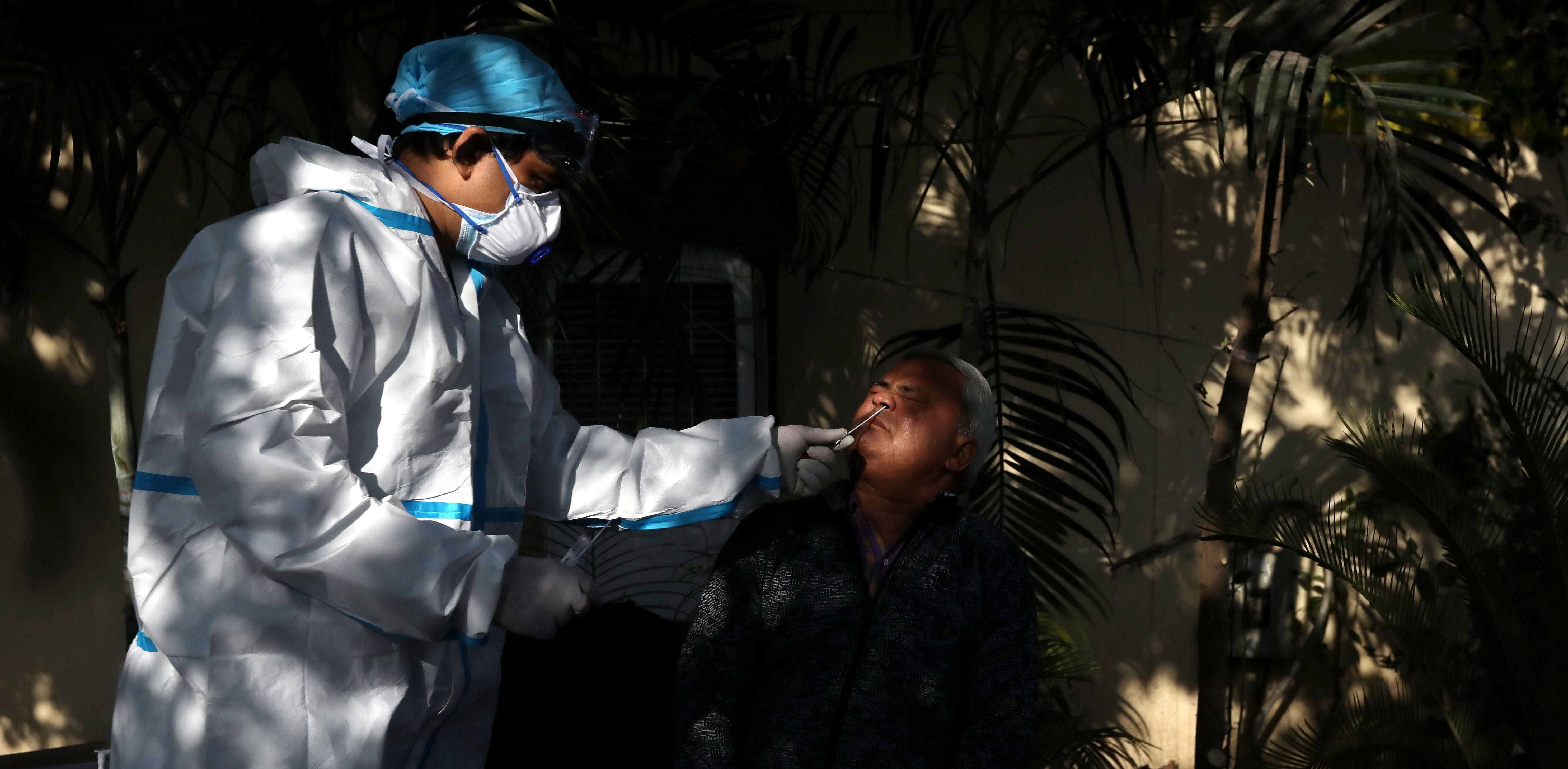 A healthcare worker wearing personal protective equipment (PPE) collects a swab sample from a man amidst the spread of the coronavirus disease (COVID-19), at a bus depot in New Delhi. Credit: Reuters