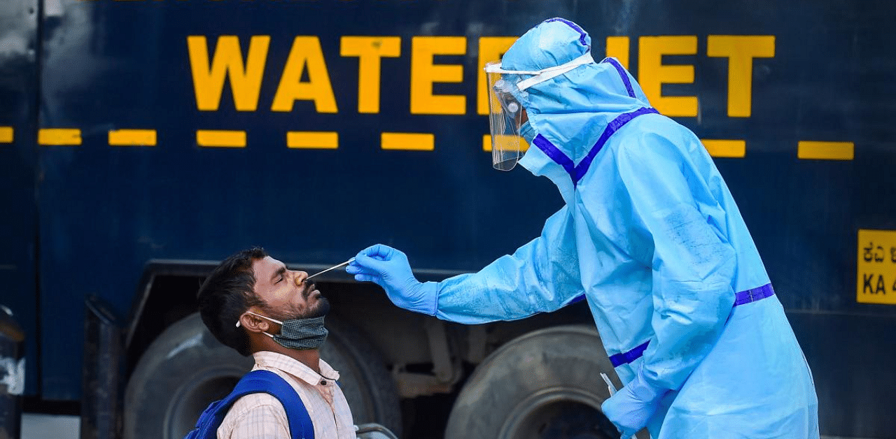 A health worker collects swab sample of a passenger for the Covid-19 test at the KSRTC bus stand in Bengaluru. Credit: PTI