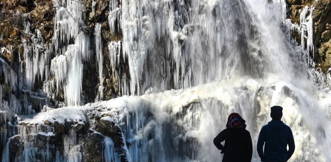 A couple looks at a partially frozen waterfall, at Tangmarg in Baramulla District, Wednesday, Dec. 16, 2020. Kashmir valley recorded its coldest night recently as the temperature dropped below zero. Credit: PTI Photo