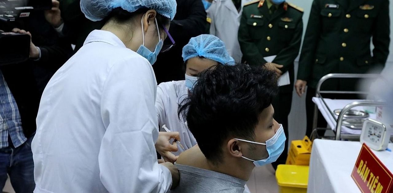 This picture taken and released by the Vietnam News Agency on December 17, 2020 shows Vietnamese military medical officials (L) giving a shot of the Covid-19 vaccine Nanocovax, developed by Vietnamese pharmaceutical firm Nanogen, to a volunteer (R) during the start of human trials at the Military Medical University in Hanoi. Credit: AFP.