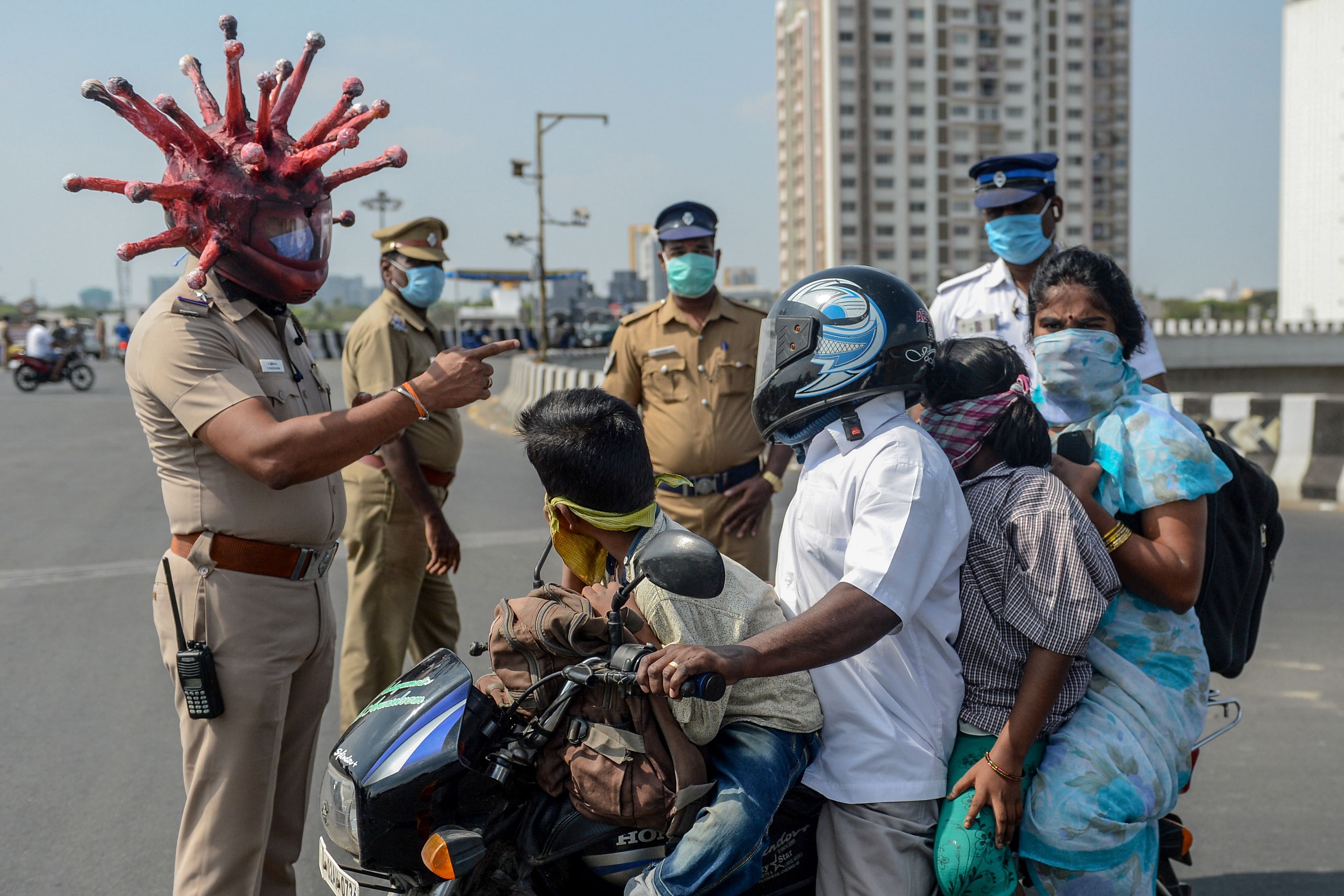 Police inspector Rajesh Babu (C) wearing coronavirus-themed helmet speaks to a family on a motorbike. Credit: AFP Photo