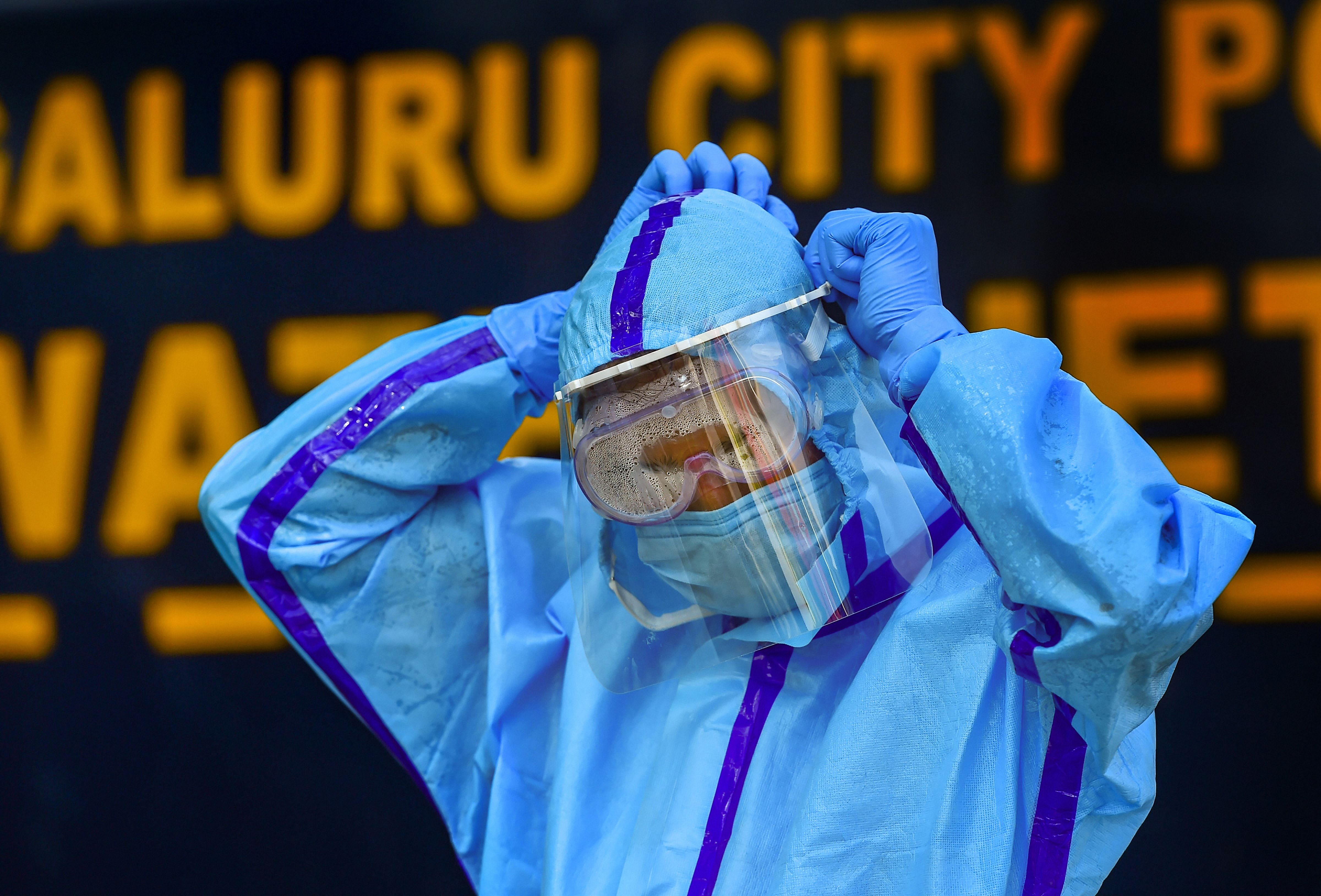 A health worker adjusts his face shield as he prepares to collect swab samples of passengers for the COVID-19 test at KSRTC bus stand in Bengaluru, Monday, Dec. 14, 2020. Credit: PTI Photo