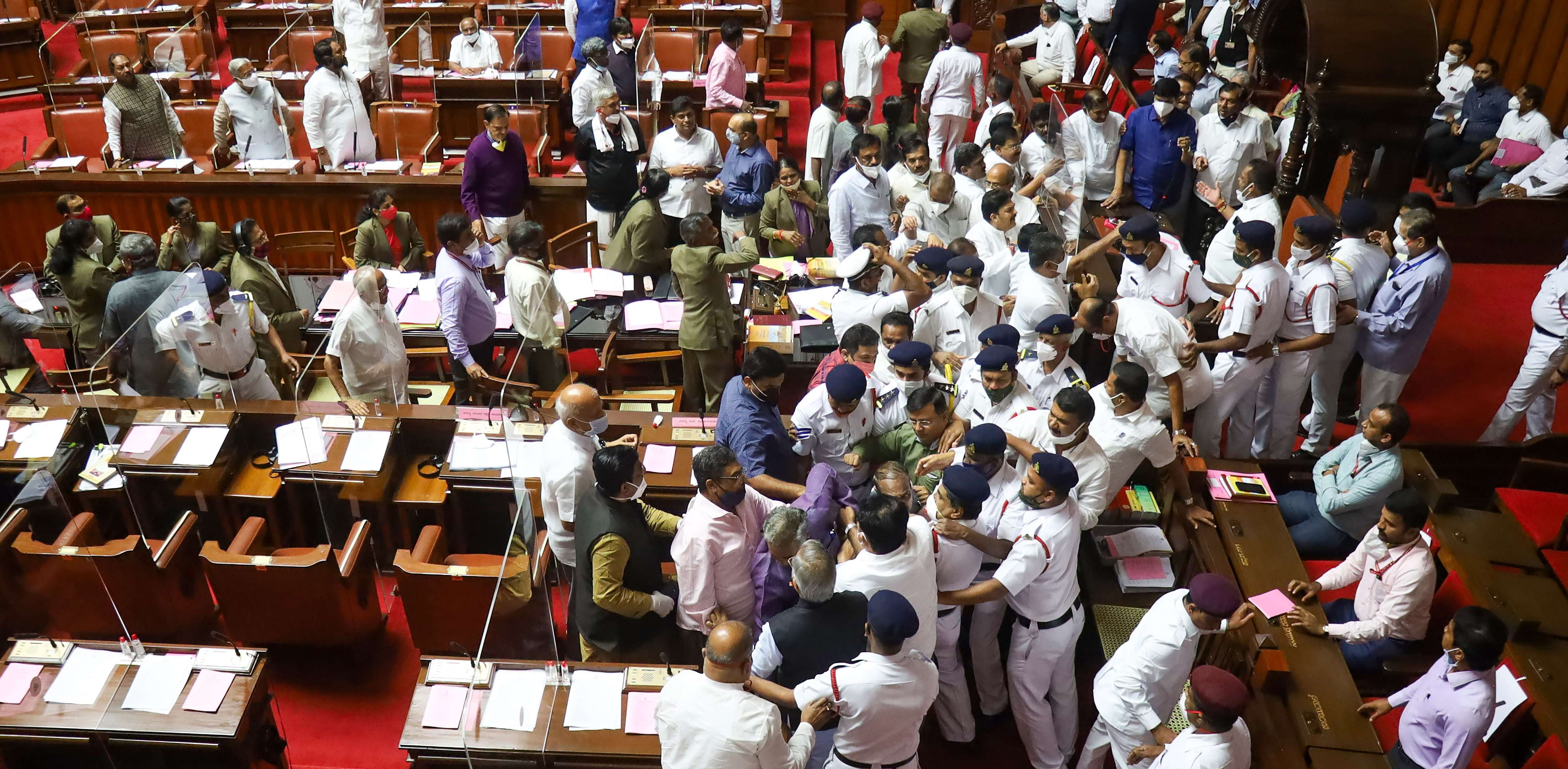 Security personnel attempt to stop ruckus between BJP and Congress leaders, which broke out over the chairman post, during the Karnataka Legislative Council in Bengaluru. Credit: PTI