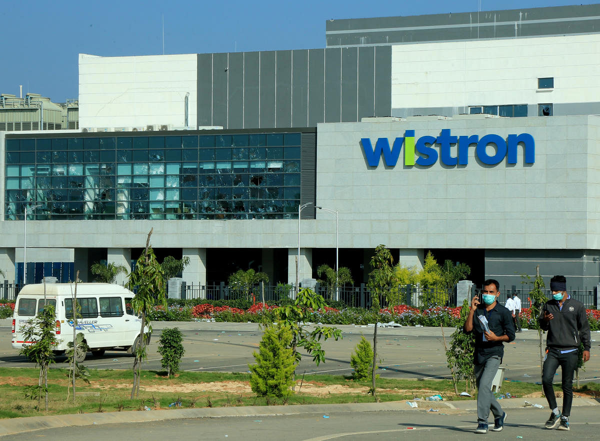 Men wearing protective face masks walk past broken windows of a facility run by Wistron Corp, a Taiwanese contract manufacturer for Apple, in Narsapura. Credit: Reuters photo. 