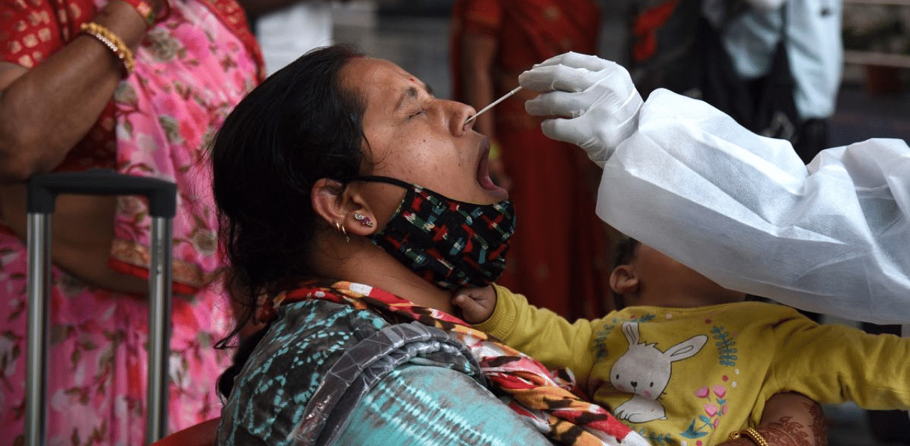 A health worker (R) takes a nasal swab of a passenger for a Covid-19 coronavirus RT PCR and Rapid Antigen test at a railway platform in Mumbai. Credit: AFP