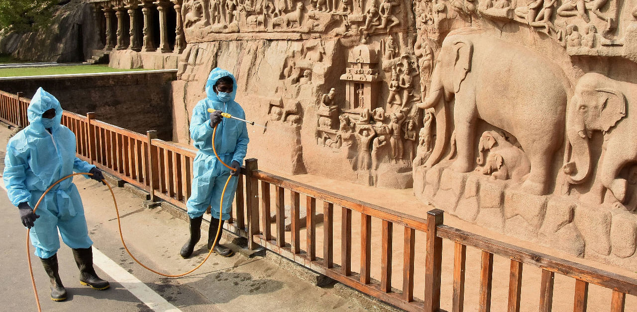 Workers wearing PPE spray disinfectants at rock carvings of Mamallapuram after the monuments opened for public. Credit: PTI Photo