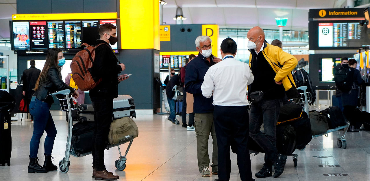 Travellers wearing a face mask or covering due to the COVID-19 pandemic, stand at check-in desks at Terminal 2 of Heathrow Airport. Credit: AFP Photo