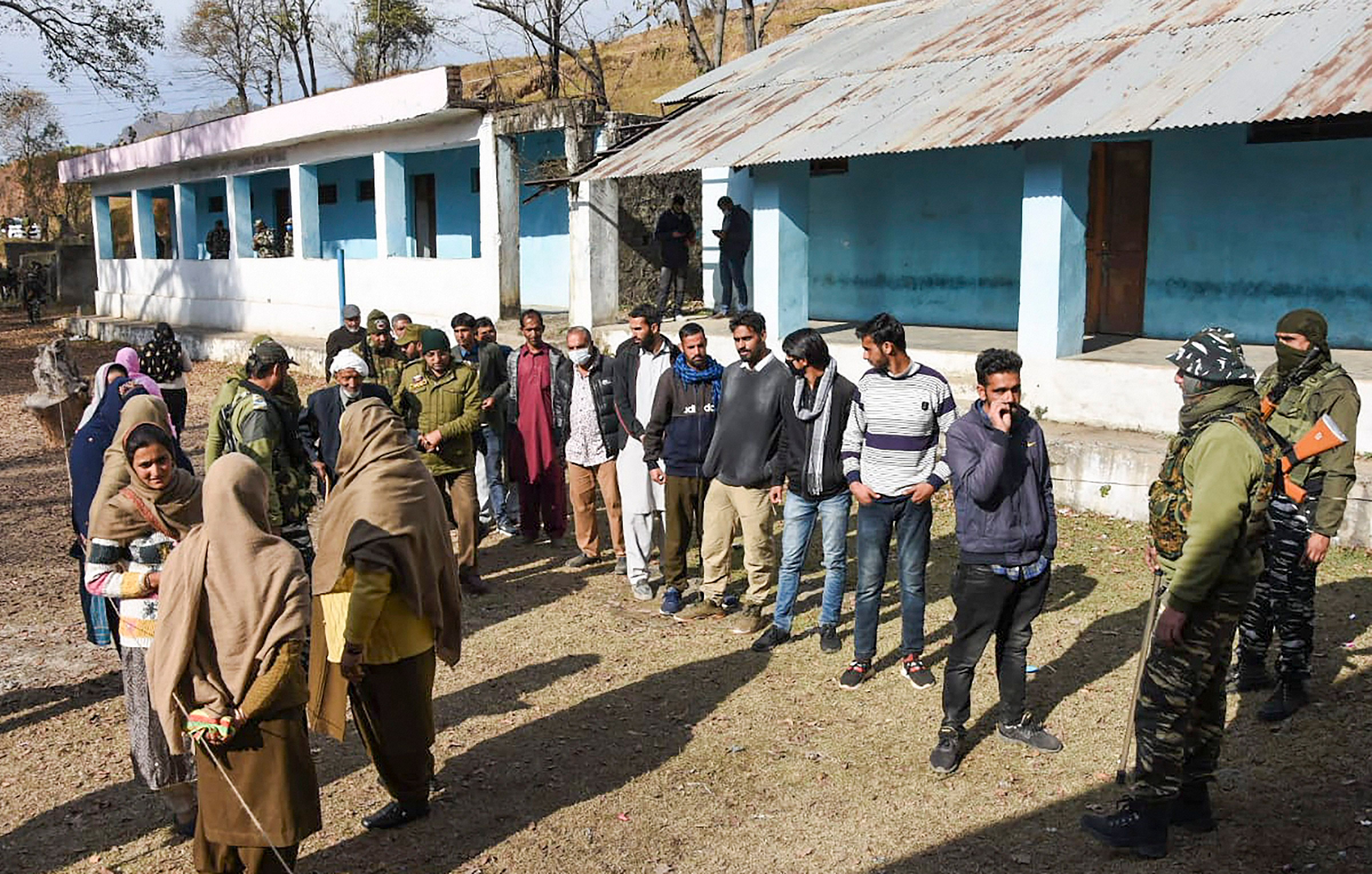 Security personnel stand guard as residents queue to cast their votes during re-polling of DDC elections. Credit: PTI Photo