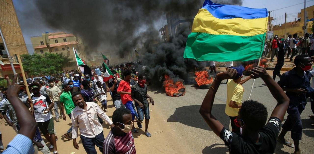In this file photo taken on June 30, 2020, Sudanese demonstrators wave Sudan's independence-era flag (R) as smoke billows from burning tyres during a protest in Khartoum. Credit: AFP.