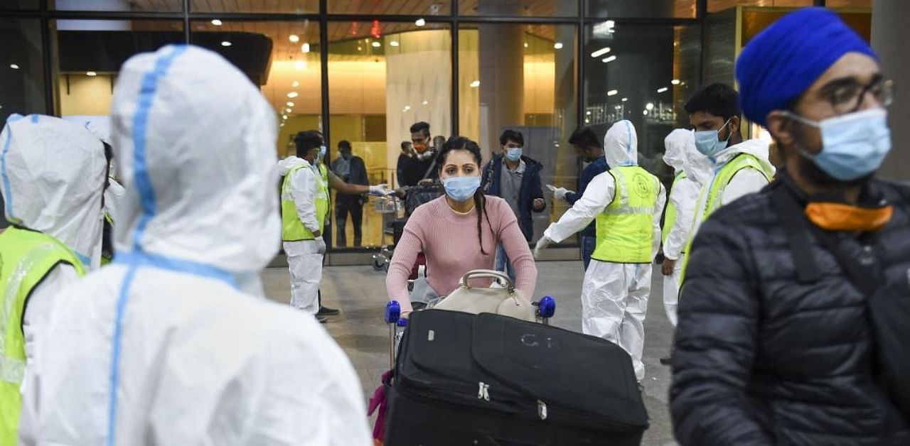 Municipal workers in personal protective equipment look on as passengers from United Kingdom arrive at the Chhatrapati Shivaji Maharaj International Airport, in Mumbai, Tuesday, Dec. 22, 2020. Credit: PTI Photo