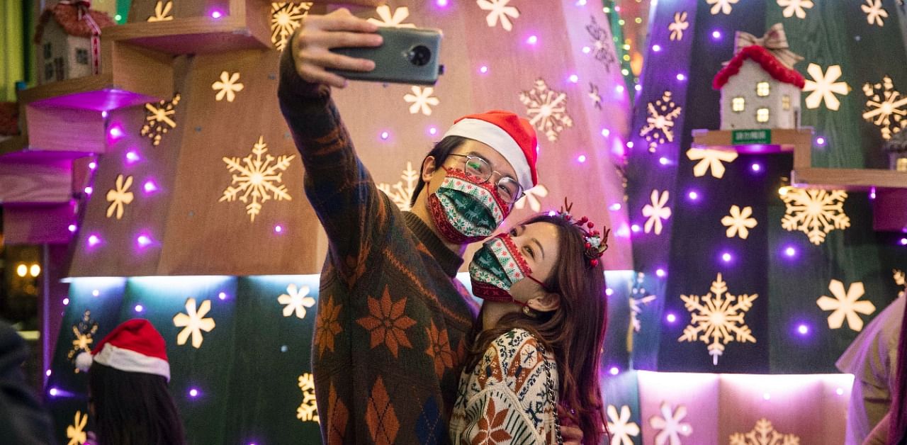 A couple wearing protective masks to prevent the spread of coronavirus, take a selfie in front of Christmas decorations in Hong Kong. Credit: AP/PTI Photo