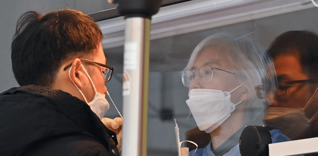 A medical staff member (R) wearing protective gear takes a swab from a visitor to test for Covid-19 at a temporary testing station outside the City Hall in Seoul. Credit: AFP File Photo