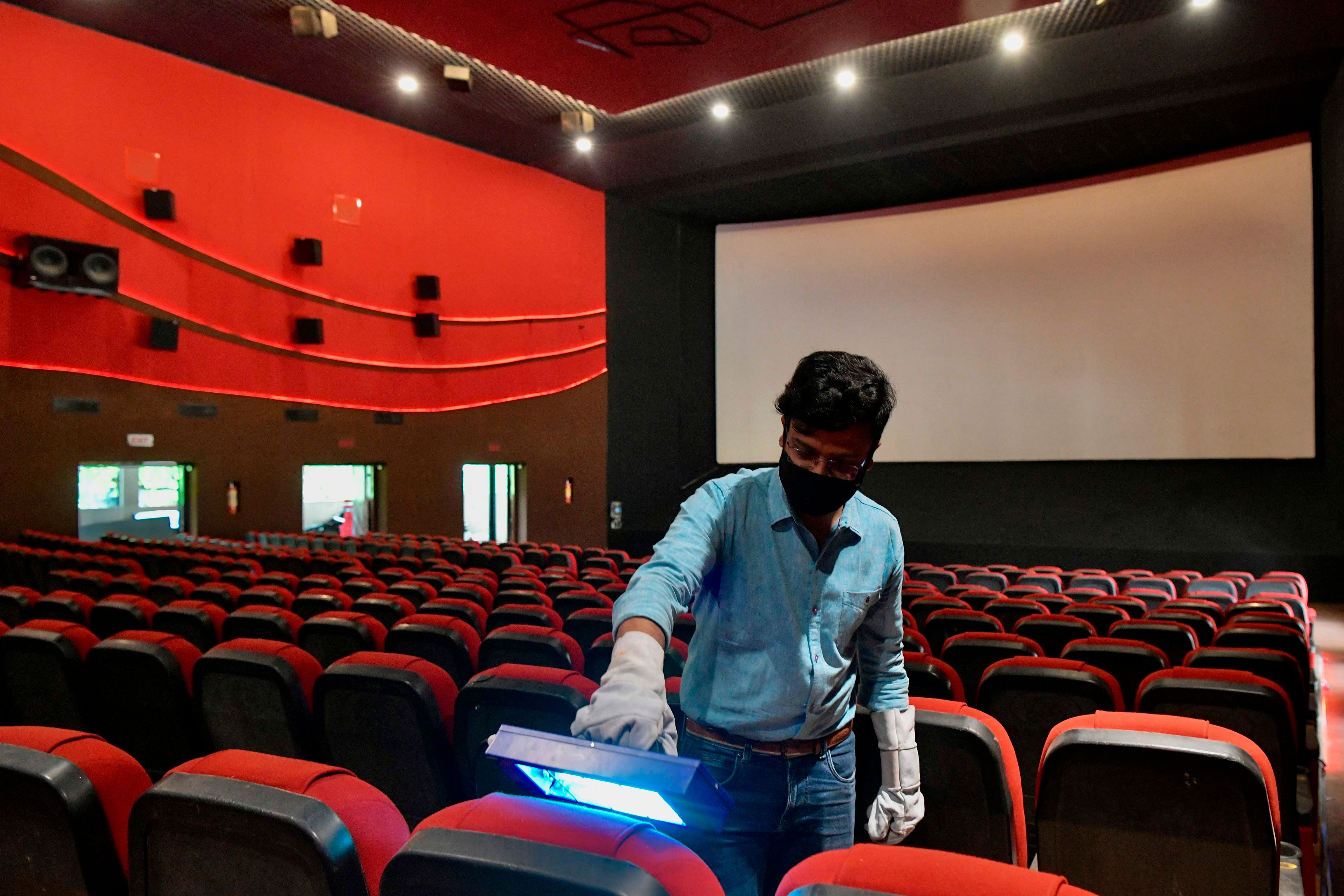A vendor (L) demonstrates the sterilisation process with an ultraviolet light device on cinema theatre seats in Bangalore on October 8, 2020 as cinemas prepare to reopen on October 15 at 50 percent seating capacity after closing due to the Covid-19 coronavirus pandemic. Credit: AFP File Photo