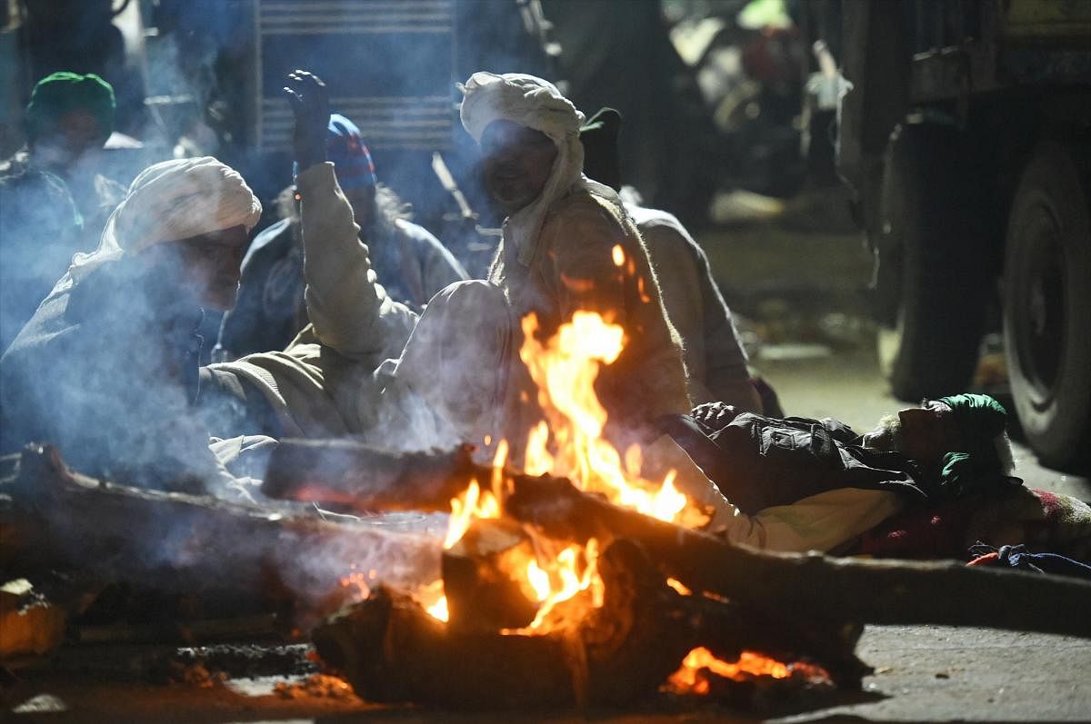 Farmers sit near a bonfire to warm themselves on a cold winter night during their protest against the new farm laws, at Ghazipur border in New Delhi. Credit: PTI. 