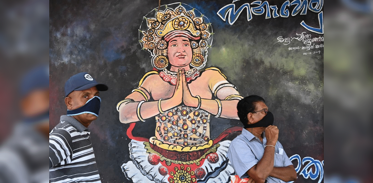 People wearing protective facemasks stand in front of a mural during a nationwide curfew imposed as a preventive measure against the spread of the COVID-19 novel coronavirus in Piliyandala on the outskirts of Sri Lanka's capital city Colombo on April 2, 2020. Credit: AFP Photo