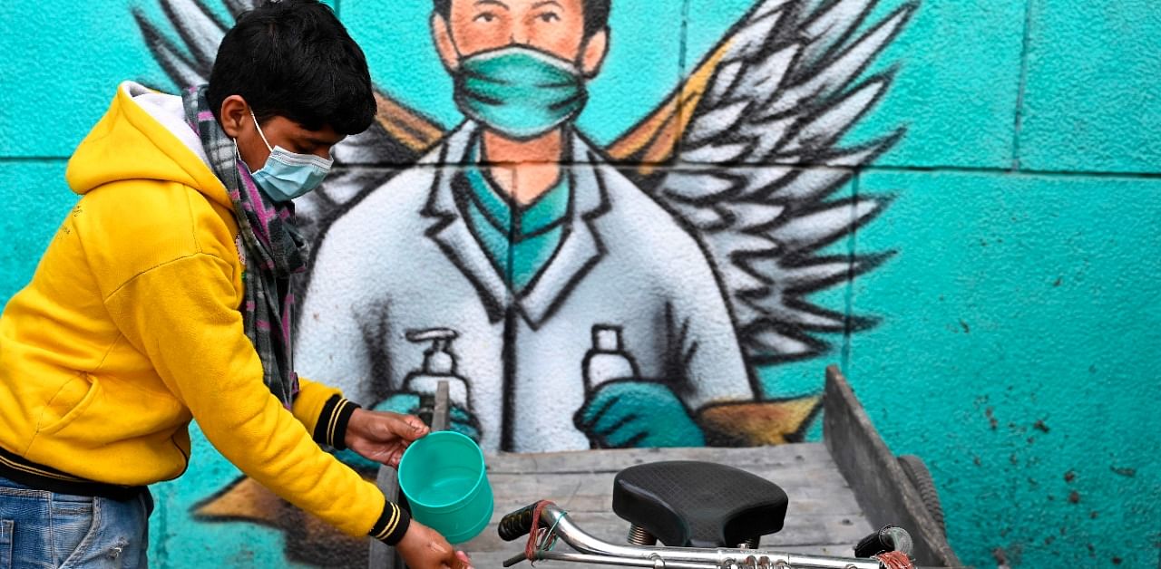 A vendor of a roadside eatery stall washes his hands in front of a mural representing a frontline warrior of the Covid-19. Credit: AFP Photo