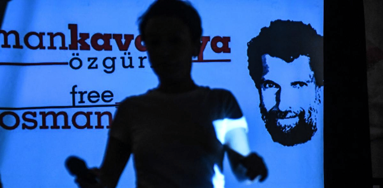 An attendee passes in front of a screen featuring an image of jailed businessman and philanthropist Osman Kavala during a press conference held by his lawyers in Istanbul. Credit: AFP Photo
