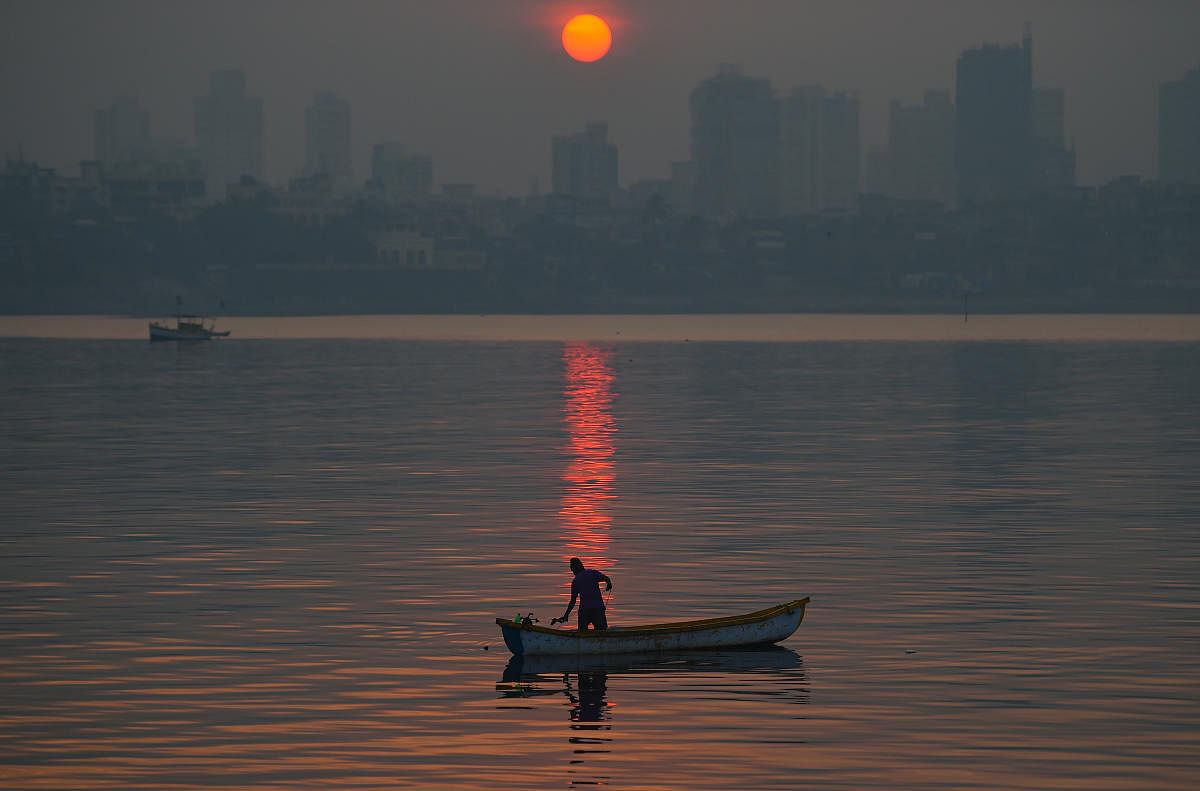 A fisherman fishes in the sea water as smog engulfs the city skyline, in Mumbai, Saturday, Dec. 26, 2020. Credit: PTI Photo