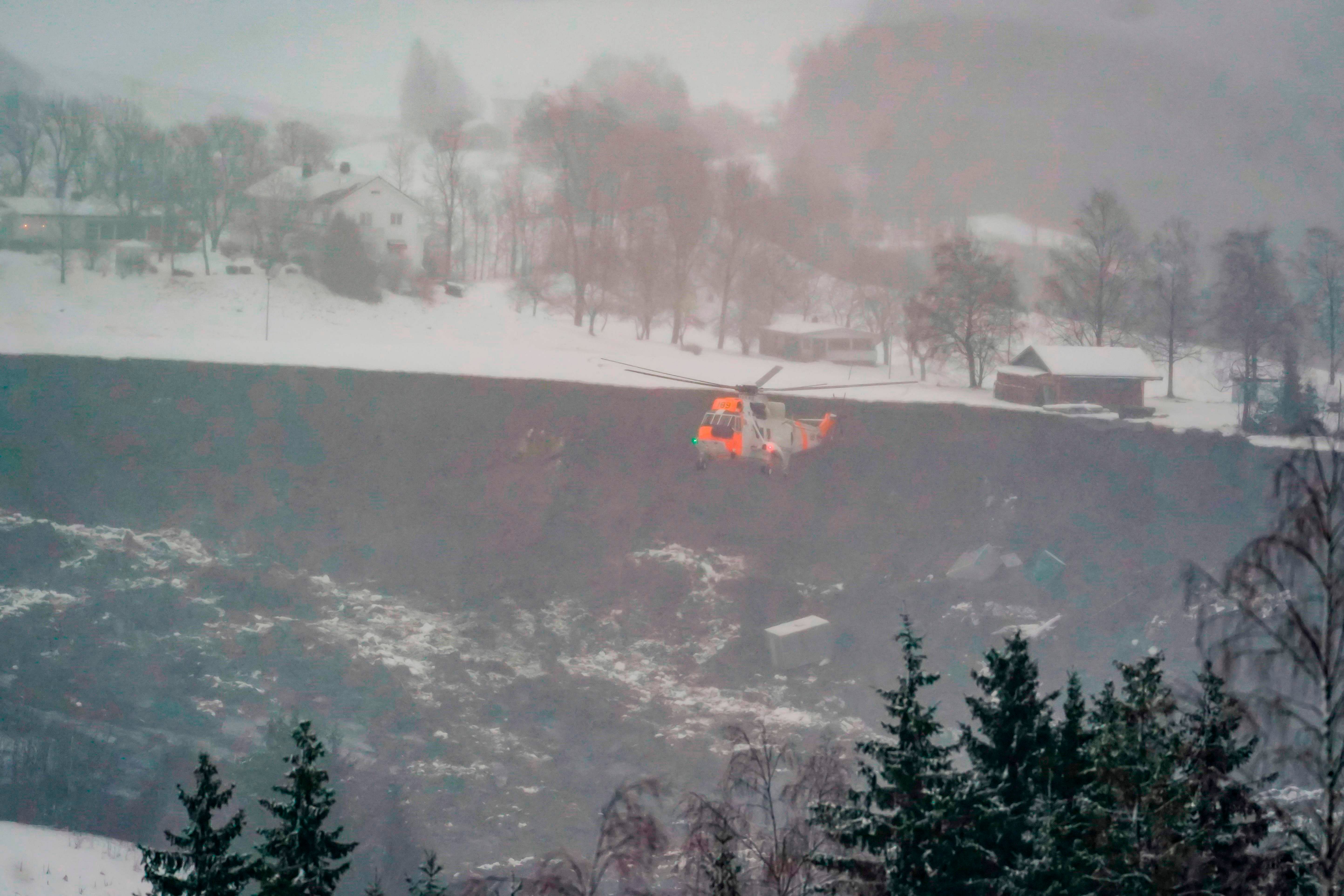 A rescue helicopter flies above debris from destroyed houses seen in a ravine created by a landslide in the town of Ask, Gjerdrum county, some 40 km northeast of the Norwegian capital Oslo. - Several houses were taken by a landslide in the early hours of December 30, several injured were taken to hospital for treatment and yet more people are listed as missing as the rescue mission continues. Credit: AFP Photo