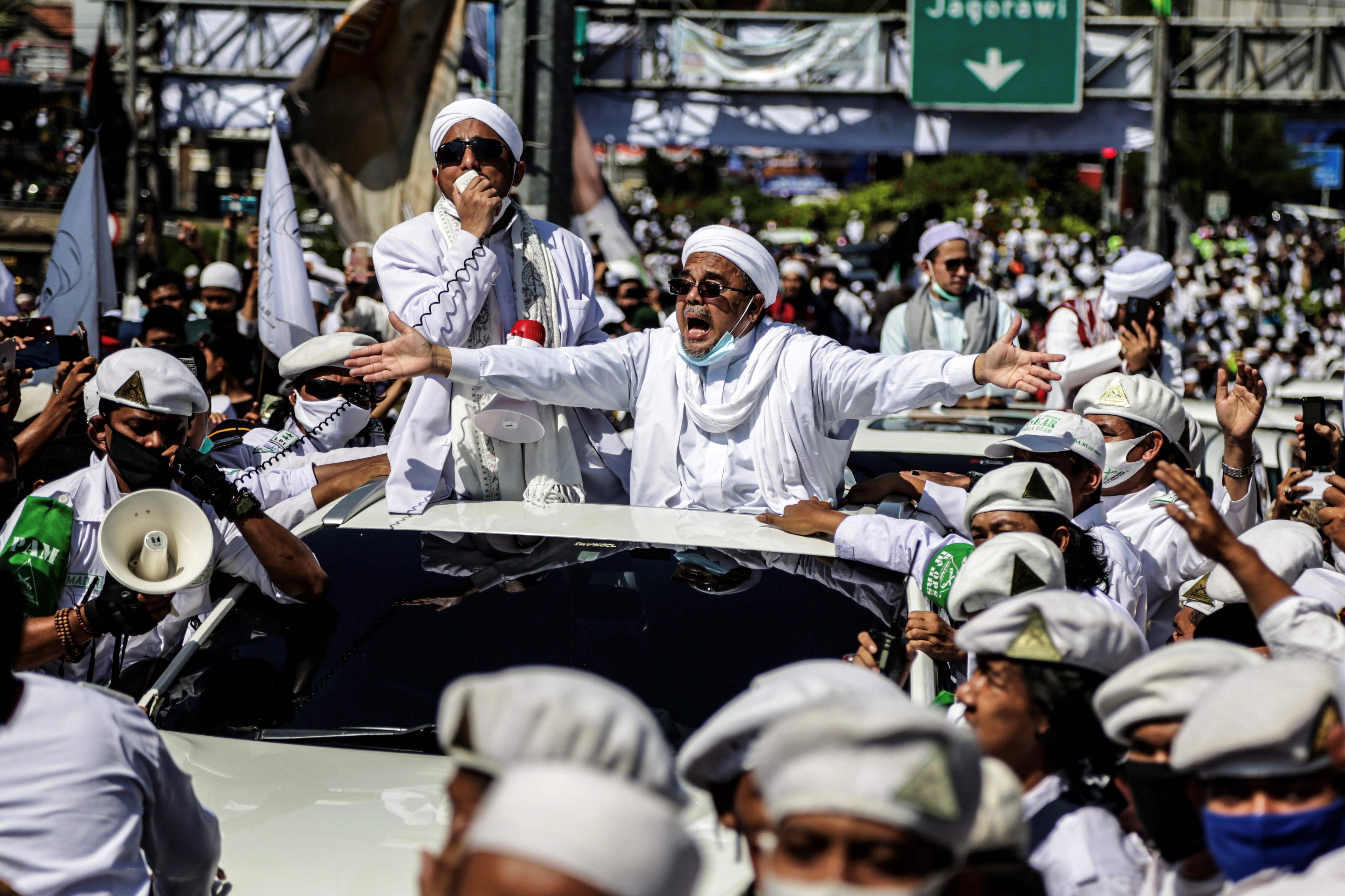 In this file photo taken on November 13, 2020, Muslim cleric Rizieq Shihab (C), leader of the Indonesian hardline organisation FPI (Front Pembela Islam or Islamic Defenders Front), gestures to supporters as he arrives to inaugurate a mosque in Bogor. - Indonesia has banned an influential hardline Islamic group as police held its leader in custody over allegations he violated virus protocols by holding mass gatherings, the country's chief security minister said on December 30, 2020. Credit: AFP Photo