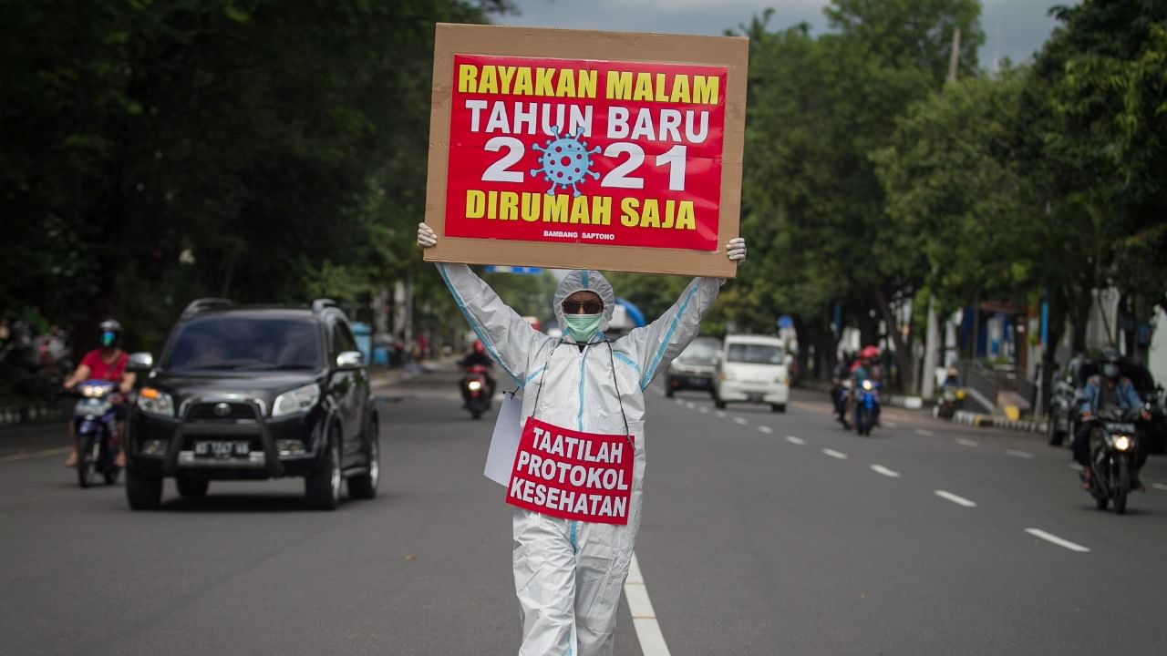 A man wearing protective gear holds a sign reading “Celebrate New Year's Eve 2021 at home” and “adhere to health protocols” at the Solo, Central Java Province. Credit: Reuters Photo